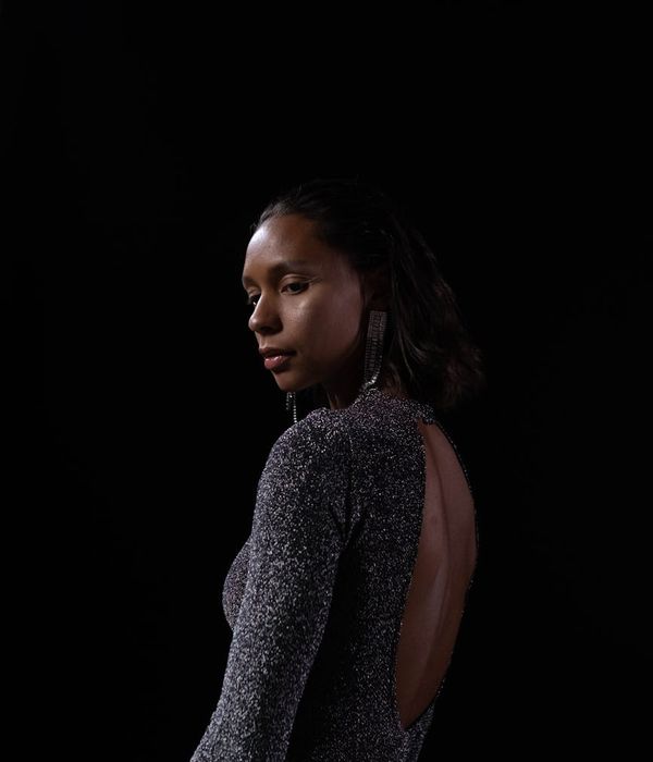 Woman holding a complex yoga balance pose in a dark studio with golden light.